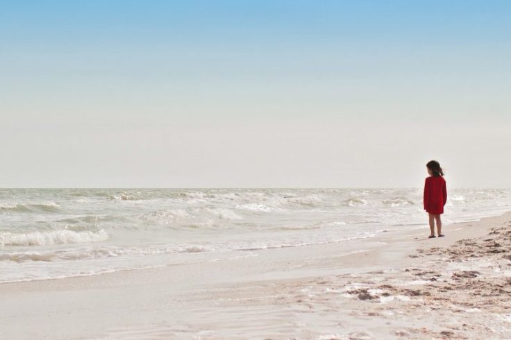 bambina in spiaggia davanti alle onde del mare